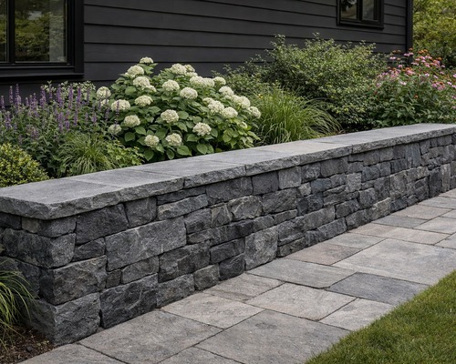 Raven Hill stone garden wall beside a paved walkway and flowering plants.